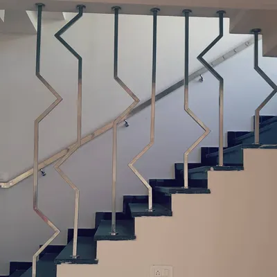 This custom staircase railing features a modern, geometric design made of stainless steel. The zig-zag pattern creates a strong visual line that is both a safety feature and a sculptural element within the home's interior.