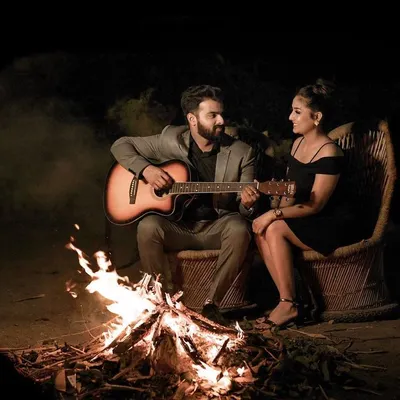 A pre-wedding shoot set against a crackling bonfire at night. The groom plays the guitar for his fiancée, creating a warm, intimate, and cinematic scene perfect for a couple's love story film.