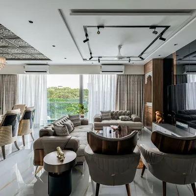A wide view of a luxurious open-plan living and dining area in a Mumbai 4BHK. The design features distinct zones for lounging and dining, unified by elegant furniture, track lighting, and a grand chandelier, creating a perfect setting for family life and social gatherings.