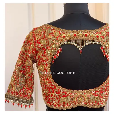 A truly unforgettable statement back. This red bridal blouse features a bold heart-shaped cutout, heavily outlined with gold zardozi and finished with hanging pearl and red bead tassels.