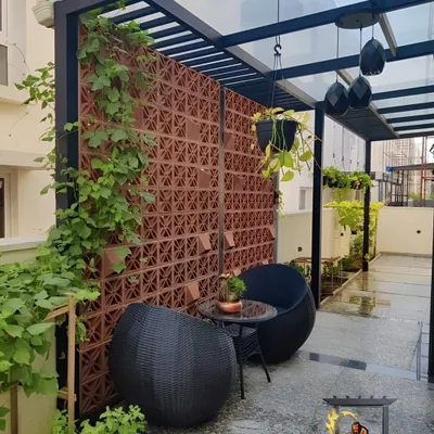 This cozy patio corner demonstrates how we integrate different elements. We installed a glass pergola for rain protection and a terracotta jali wall for privacy and airflow, creating a comfortable and secluded outdoor seating nook.