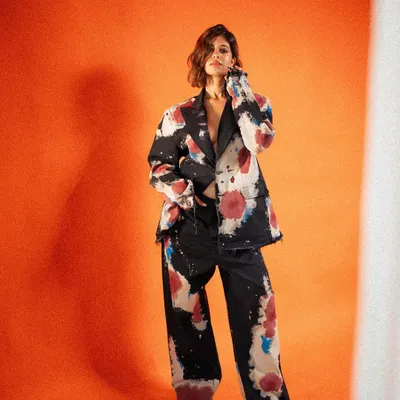 A full-length shot for an Apple campaign with Sejal Kumar, featuring a hand-painted suit by Huemn. The bold orange background makes the artistic outfit pop, creating a powerful and fashion-forward image.