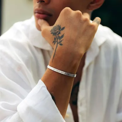 A man wearing a silver cuff bracelet engraved with a set of coordinates. This is a popular choice for remembering a favorite travel spot, a hometown, or where a special event happened.