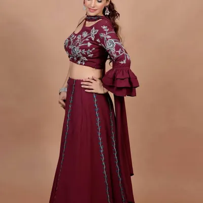 This wine-colored indo-western lehenga features a stylish one-shoulder blouse with bell sleeves and beautiful embroidery. It's a perfect blend of modern trends and ethnic charm.