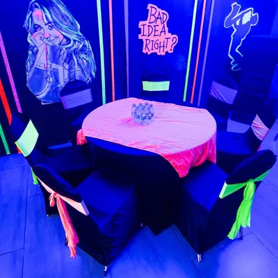 A seating area transformed by blacklight, with neon chair sashes and glowing wall art creating an immersive, high-energy vibe.