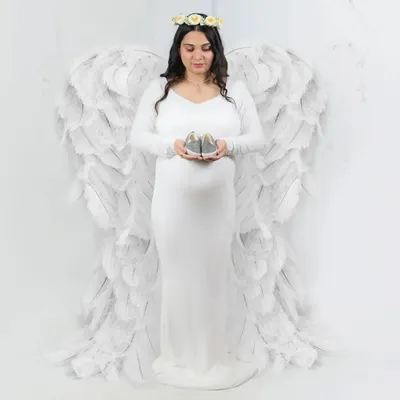 For a truly memorable and symbolic portrait, I offer these beautiful, large angel wings. Paired with a simple white gown, this setup creates a powerful and angelic image of motherhood. Here, the mother holds a pair of baby shoes, adding a touch of sweet anticipation.
