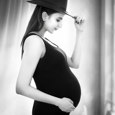 A modern and stylish black and white portrait. The addition of a fedora hat adds a touch of personality and fashion-forward flair to this classic maternity shot.