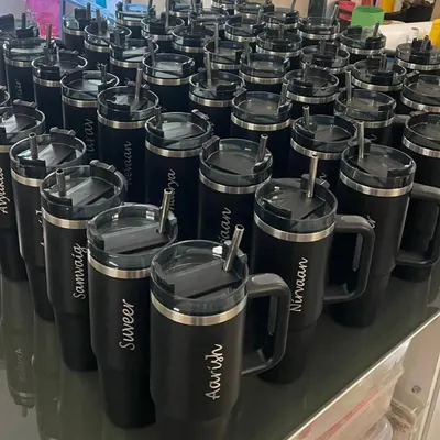 We handle bulk orders with precision and style. This image shows a large batch of personalized black tumblers, each engraved with a name, ready for a corporate event or a large party.
