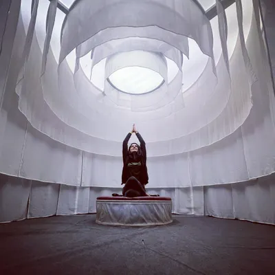Finding stillness in Gomukhasana, or cow face pose, within a serene meditation space. The circular white drapes create a cocoon-like feeling, perfect for turning your focus inward.
