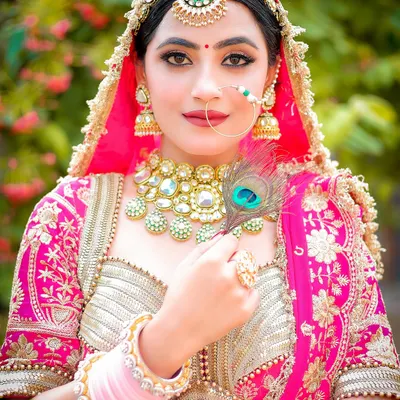 A stunning close-up of a bride in her pink lehenga, holding a peacock feather. I pay close attention to details like the maang tikka, nath, and heavy necklace, ensuring every element of the bridal look is captured perfectly.