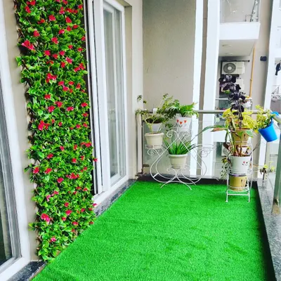 A complete balcony makeover. I installed a soft artificial grass floor and a vibrant vertical garden wall with red flowers, instantly adding color and life to the space.