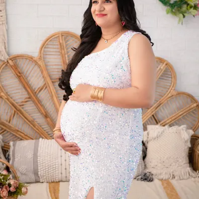 A moment of quiet confidence. Here, the mother-to-be glows in a white sequin mermaid gown, her pose highlighting the beautiful silhouette of pregnancy against our boho-chic studio set.