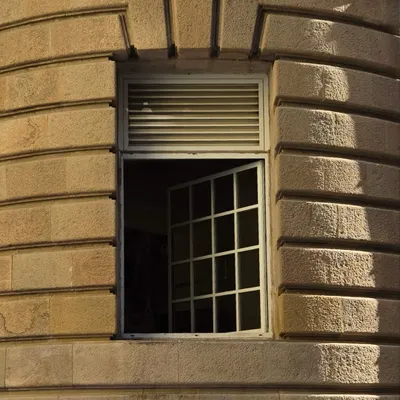 A close-up of a window in a stone building in Fort, Mumbai. The play of light and shadow on the gridded pane and louvered shutter is just perfect.