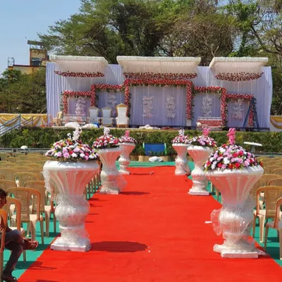 A full view of an outdoor wedding reception stage I designed. The setup includes a multi-level white stage, extensive floral decorations with roses, and a perfectly laid red carpet aisle for a grand and memorable event.
