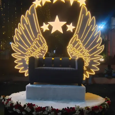 This is a custom-designed photo booth or stage backdrop featuring large, illuminated angel wings and stars. It creates a glamorous and celestial focal point for any evening event, perfect for couple or guest photos.