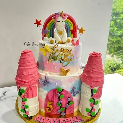 A magical unicorn castle cake for a 5th birthday. This two-tier design features buttercream towers, a whimsical unicorn, and a rainbow, creating a complete fairytale scene.
