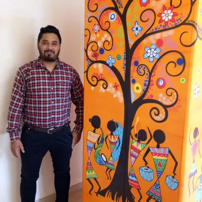 This plain steel cupboard was transformed with a vibrant and colorful Warli painting. This traditional art form, depicting dancing figures around a tree, turns a functional item into a beautiful and unique piece of decor.