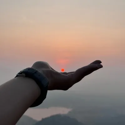 A creative shot of a trekker holding the rising sun in their palm at Uttari Betta.