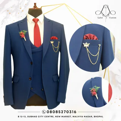 A classic navy blue three-piece suit, perfectly styled with a bold red tie and matching pocket square. The details, like the floral lapel pin and crown brooch, show how we can personalize a timeless look for a wedding or formal event.