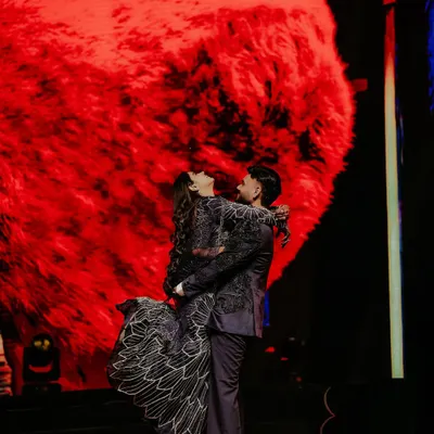 A classic romantic pose on the Sangeet stage. The groom lifts his bride against a giant, glowing red heart, creating a dramatic and iconic shot that’s perfect for a night of celebration.