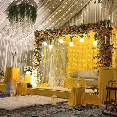 This stage setup for a Haldi ceremony combines a bright yellow backdrop with lush marigold and sunflower arrangements. The hanging lights and white lanterns add a touch of modern elegance to the traditional theme, creating a warm and inviting focal point.