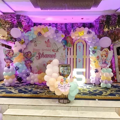 An enchanting fairy-themed stage decoration for a 5th birthday. This setup includes a custom backdrop, pastel balloon arrangements, fairy cutouts, and a large light-up number '5'.