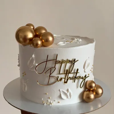 Simplicity at its finest. This all-white whipped cream cake is decorated with a "Happy Birthday" topper and delicate gold spheres for a clean, modern, and elegant look.