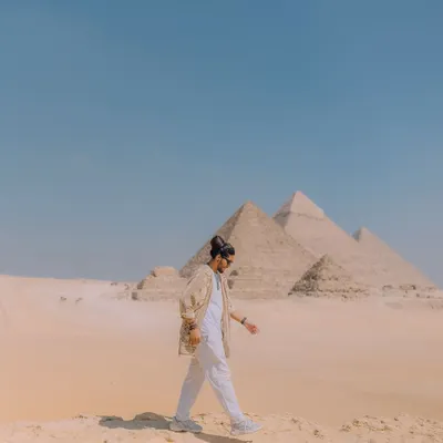 Walking across the sands of Giza with the pyramids in the distance. This wide shot captures the immense scale of the landscape and the feeling of being a small part of a grand history.