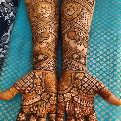 This bridal design is a testament to timeless elegance, featuring intricate shield motifs with custom initials. The combination of delicate floral patterns and geometric jaali work creates a rich, balanced look perfect for a bride.