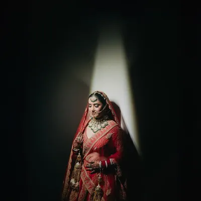 A stunning bridal portrait of Shreya, using a single beam of light to create a dramatic, high-fashion effect. This technique highlights her features and the richness of her red lehenga, turning a photo into a piece of art.