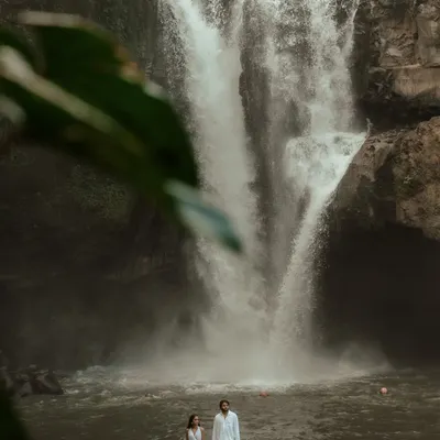 An epic shot of a couple standing before a majestic waterfall in Bali. This image captures the power of nature and the spirit of adventure, showing the scale of the landscape and the couple's place within it.