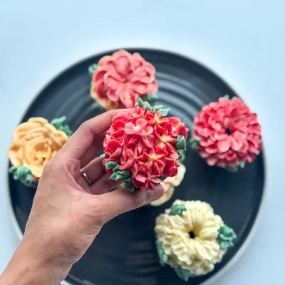 Holding up a detailed red hydrangea cupcake, crafted entirely from buttercream.