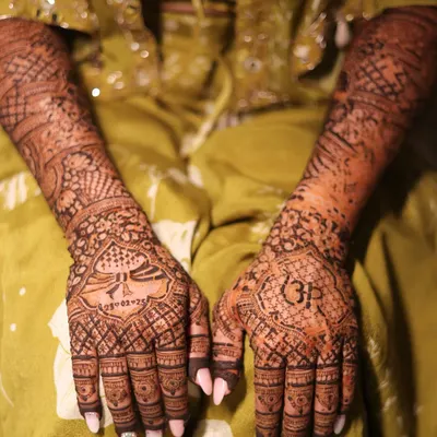The complete bridal look, with both hands adorned in intricate, personalized mehendi. This design features portraits, initials, and traditional patterns.