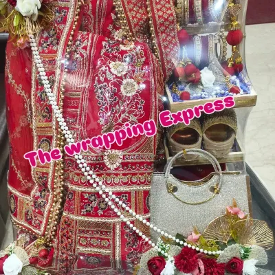A close-up of a beautifully packed red bridal lehenga. You can see the detailed embroidery, and I've arranged the matching handbag, juttis, and bridal chooda to create a complete and impressive gift set.