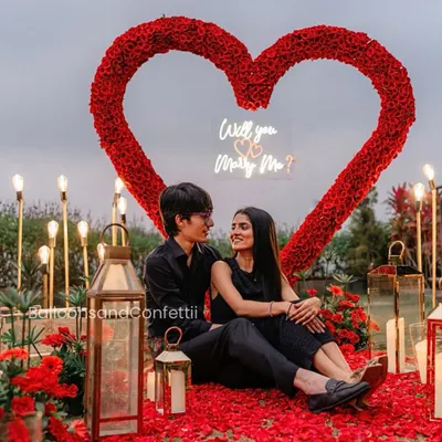 The ultimate romantic gesture. This proposal setup features a custom-made heart archway using over 2,000 fresh red roses, a petal-strewn floor, and a neon "Will you Marry Me?" sign for a truly unforgettable moment.