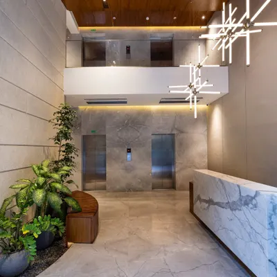 This lobby is a statement of quiet luxury, where bold marble, warm wood, and lush greenery come together in a balanced composition. The double-height space and sculptural chandelier are designed to elevate the arrival experience and establish a distinct spatial identity.