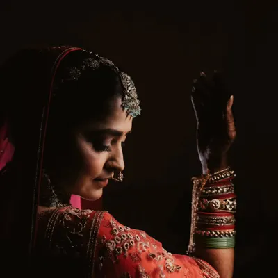 In the quiet moments before the ceremony, a bride's portrait is a story of anticipation. This low-light, artistic shot captures her grace and the intricate details of her attire.