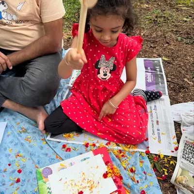 A young artist completely absorbed in the process of flower pounding. With a wooden mallet in hand, she is learning how to transfer the vibrant colours of marigold petals onto paper, creating her own unique masterpiece.