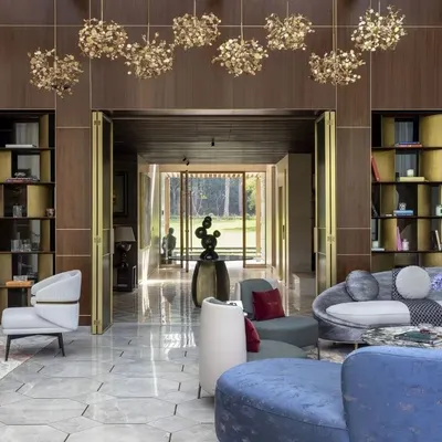 The main living area of the Vasant Kunj farmhouse, featuring a double-height ceiling, custom chandeliers, and wood paneling with brass accents. This space was designed for both grand entertaining and comfortable family living.