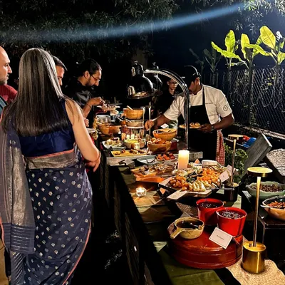 Guests enjoy a lavish spread at an outdoor evening event. A chef is seen serving directly from the beautifully lit buffet, showcasing the interactive and high-touch service that defines a Single Thread gathering.