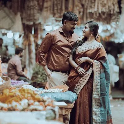 A beautiful moment in a classic Bangalore flower market. The groom-to-be looks on as his partner, dressed in a traditional saree, admires the flowers, creating a timeless, candid scene.
