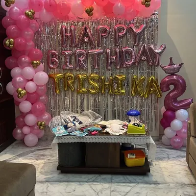 A fun and sparkly birthday setup in pink and gold. The silver fringe backdrop makes the 'Happy Birthday' foil balloons pop, and the balloon columns add a festive touch.