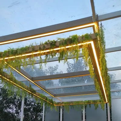 A close-up of a glass pergola I enhanced with hanging artificial creepers and warm LED strip lighting for a magical evening look.