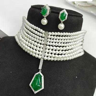 This modern multi-strand pearl choker features a central emerald green stone pendant. It comes with matching pearl drop earrings and is available for rent.