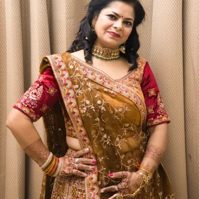A confident pose in a beautiful mustard and red embroidered lehenga. This indoor shot highlights the intricate details of the outfit and the henna on her hands.