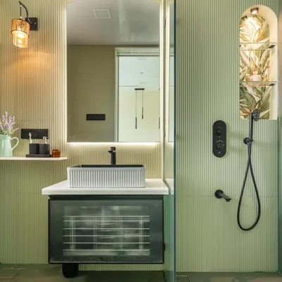 This bathroom is a serene retreat, wrapped in soft green fluted wall panels. I designed a custom niche in the shower with a tropical wallpaper backing for a surprise element. The floating vanity with a reeded glass front feels light and modern, complemented by the black matte fixtures.