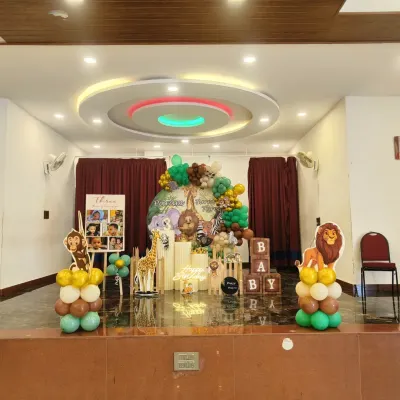 A grand jungle-themed birthday party on a stage, featuring a large balloon arrangement, animal cutouts like a lion and giraffe, and a personalized photo easel.