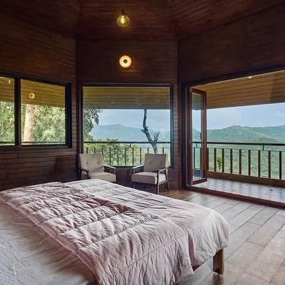 This bedroom in a rustic-luxury home is designed to be a private retreat with a connection to nature. We used wood-paneled walls and flooring to create a warm, cabin-like feel, with large windows and a private balcony that open up to stunning mountain views.