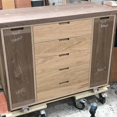 The base unit of the drinks cabinet during assembly in the workshop. This view shows the core construction, combining a birch plywood carcass with solid oak for the drawer fronts and solid walnut for the side cabinets.