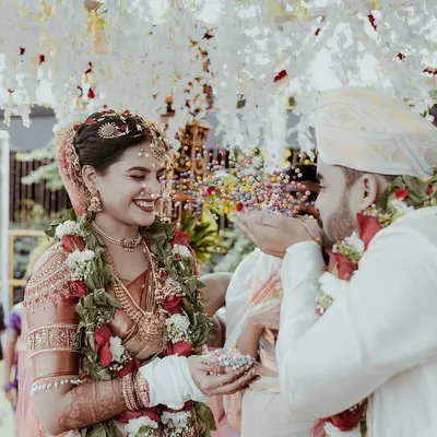 A candid shot of the groom showering the bride with blessings and rice during the ceremony. It’s a moment of pure joy and tradition, captured under a beautiful floral mandap.